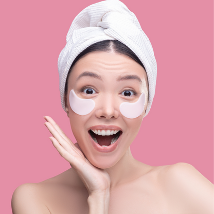Woman with eye patches and a towel on her head against a pink background